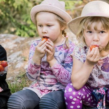 Lapset syövät metsässä tomaatteja kesäisissä vaatteissa.