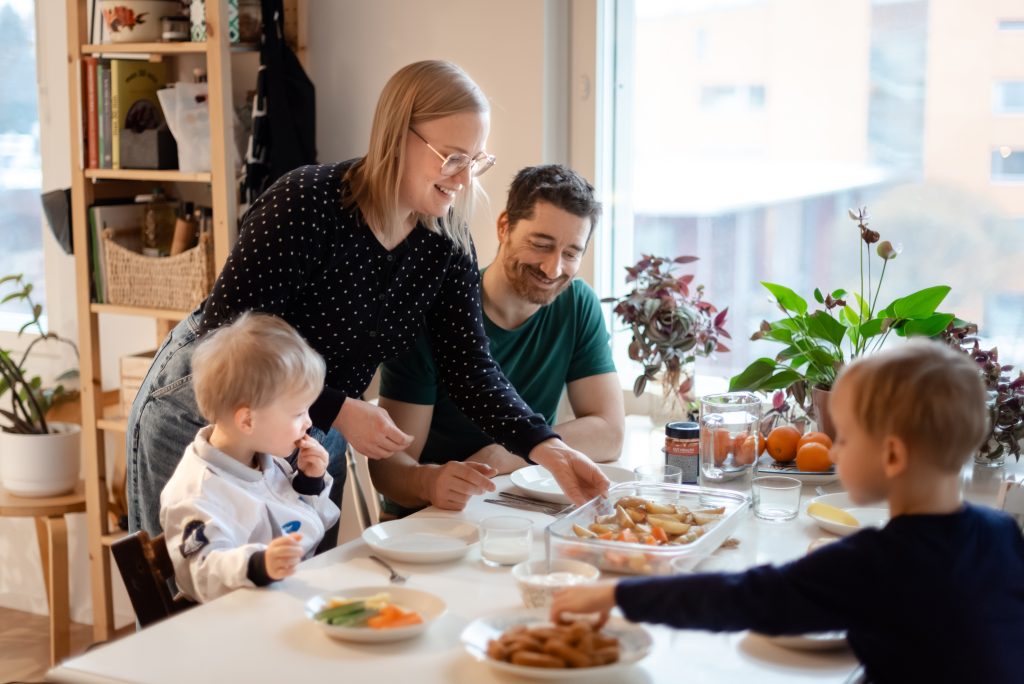 Lapsiperhe ruokailemassa yhdessä hyväntuulisina.